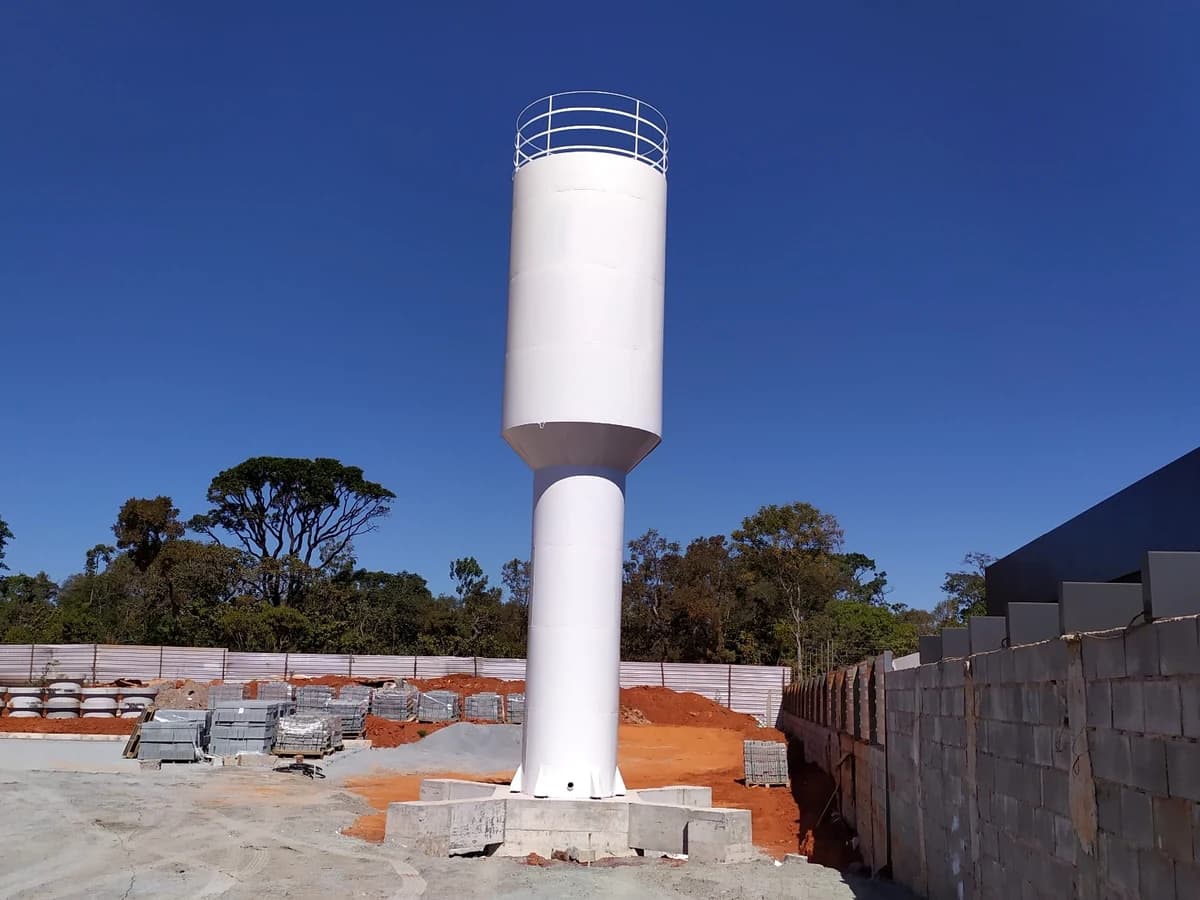 Caixa d'água metálica tipo taça coluna cheia na cor branca com guarda-corpo superior instalada sobre base de concreto